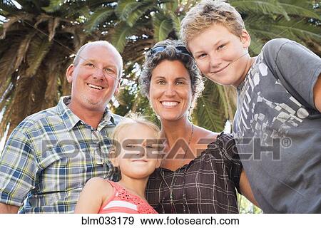 Stock Photo - Caucasian family smiling under palm tree. Fotosearch