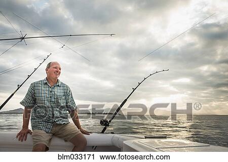 Stock Image - Caucasian man fishing from boat in ocean. Fotosearch