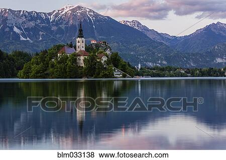 Stock Photo - Church tower and mountains reflecting in still lake. Fotosearch