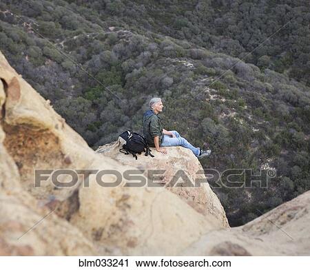 Stock Image - High angle view of older Caucasian man sitting on rock formation. Fotosearch