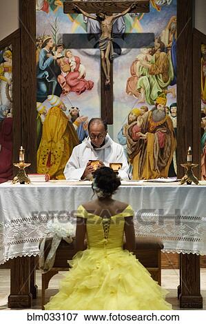 Stock Photo - Hispanic girl celebrating quinceanera with priest in Catholic church. Fotosearch