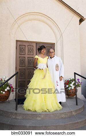 Stock Image - Hispanic priest and girl celebrating quinceanera outside Catholic church. Fotosearch