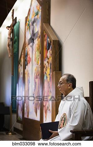 Stock Photo - Hispanic priest sitting in Catholic church. Fotosearch