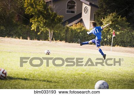 Stock Image - Mixed race boy playing soccer on field. Fotosearch