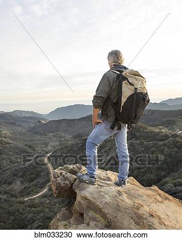 Stock Image - Older Caucasian man standing on rocky hilltop. Fotosearch