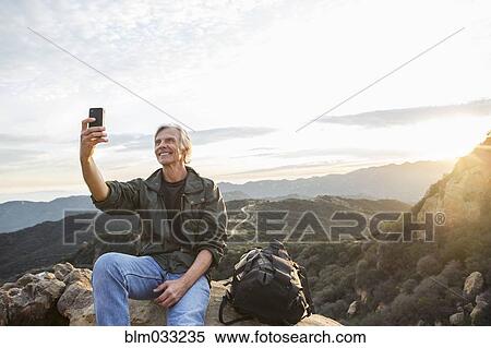 Older Caucasian man taking cell phone photograph on rocky hilltop View Large Photo Image Stock Photography - Older Caucasian man taking cell phone photograph on rocky hilltop. Fotosearch
