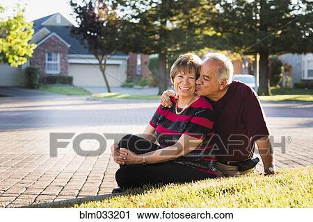 Stock Image - Older Hispanic couple kissing outside suburban home. Fotosearch