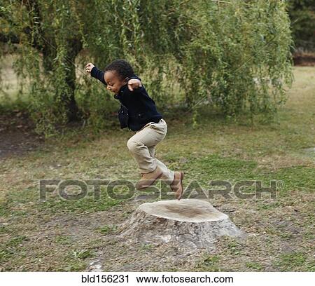 Stock Image - African American boy playing on stump in park. Fotosearch