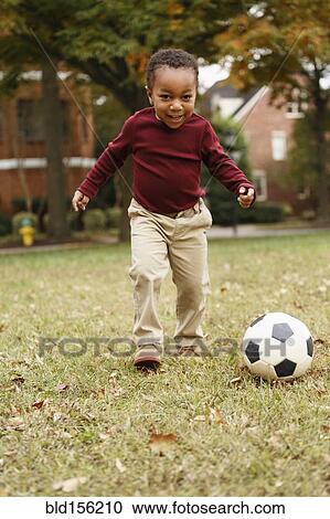 Stock Image - African American boy playing soccer in park. Fotosearch