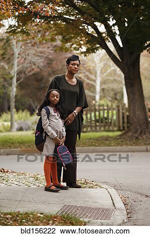 Stock Image - African American woman and daughter waiting for school bus. Fotosearch