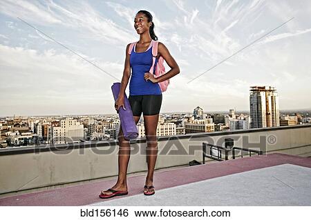 Stock Photograph - African American woman holding yoga mat on urban rooftop. Fotosearch