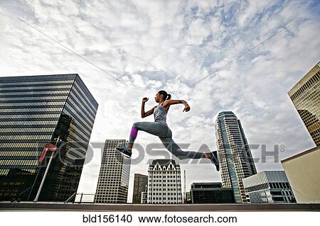 Stock Image - African American woman leaping on urban rooftop. Fotosearch
