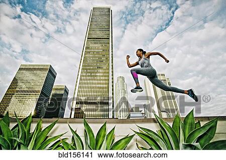 Stock Image - African American woman leaping on urban rooftop. Fotosearch