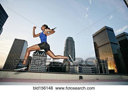Stock Photo - African American woman leaping on urban rooftop. Fotosearch