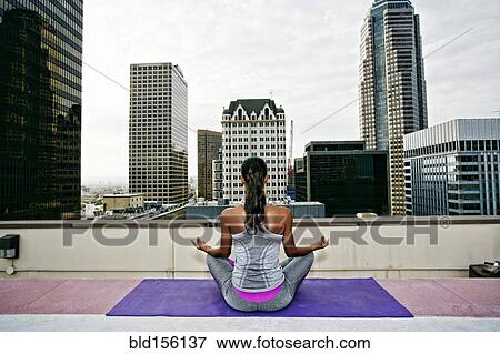 Stock Photo - African American woman meditating on urban rooftop. Fotosearch