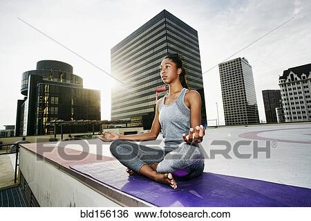 Stock Photograph - African American woman meditating on urban rooftop. Fotosearch