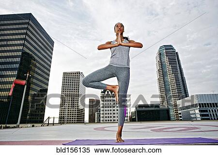 Stock Photography - African American woman practicing yoga on urban rooftop. Fotosearch