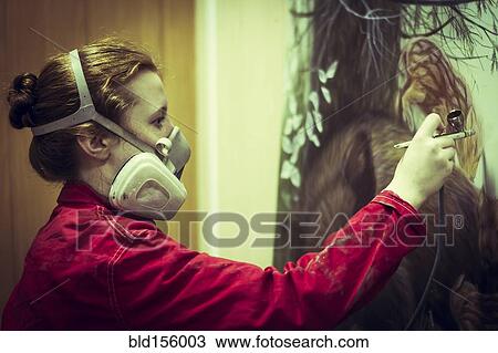 Stock Image - Artist in gas mask airbrushing painting in studio. Fotosearch