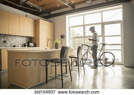 Stock Photo - Black businessman with bicycle using cell phone in office kitchen. Fotosearch
