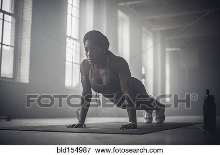 Stock Photo - Black woman doing push-ups in dark gym. Fotosearch