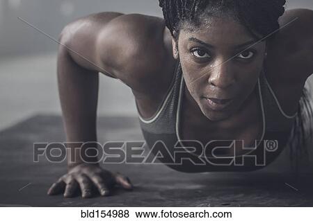 Stock Photo - Black woman doing push-ups in dark gym. Fotosearch