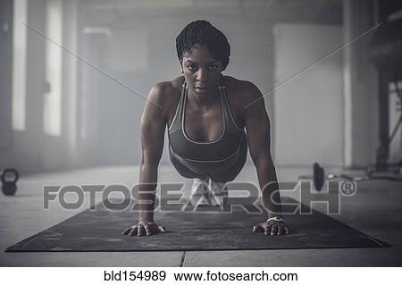 Stock Photo - Black woman doing push-ups in dark gym. Fotosearch