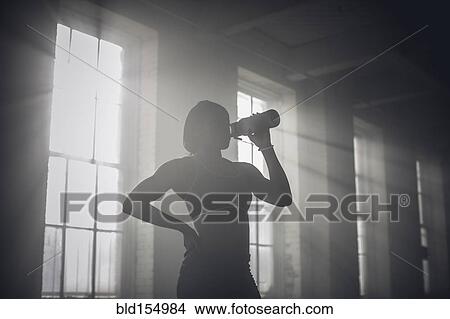 Picture - Black woman drinking water bottle in dark gym. Fotosearch