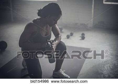 Black woman drinking water bottle in dark gym View Large Photo Image Stock Photograph - Black woman drinking water bottle in dark gym. Fotosearch