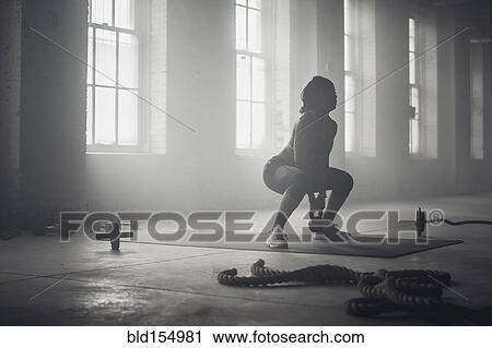 Stock Image - Black woman lifting weights in dark gym. Fotosearch