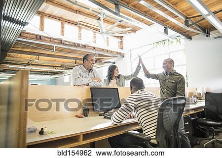 Stock Image - Business people celebrating at desk in office. Fotosearch