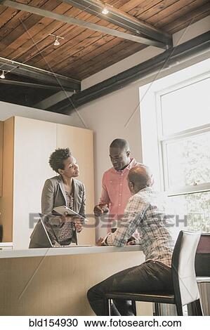 Stock Image - Business people using digital tablet in office kitchen. Fotosearch