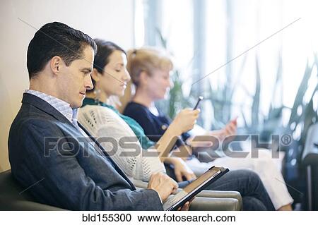 Stock Image - Business people waiting in office lobby. Fotosearch