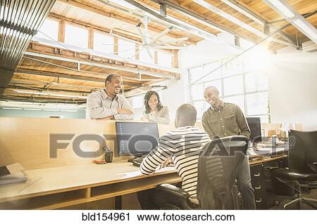 Stock Image - Business people working together at desk in office. Fotosearch