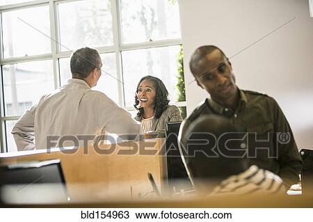 Stock Image - Business people working together at desk in office. Fotosearch