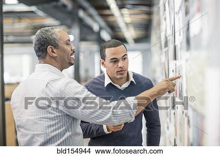 Picture - Businessmen examining photographs on wall in office. Fotosearch