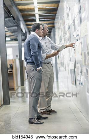 Businessmen examining photographs on wall in office View Large Photo Image Stock Photography - Businessmen examining photographs on wall in office. Fotosearch