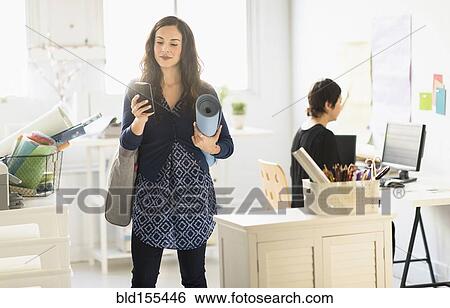 Stock Photograph - Businesswoman carrying yoga mat and cell phone in office. Fotosearch