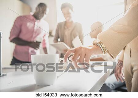 Stock Image - Businesswoman drinking cup of coffee in office. Fotosearch
