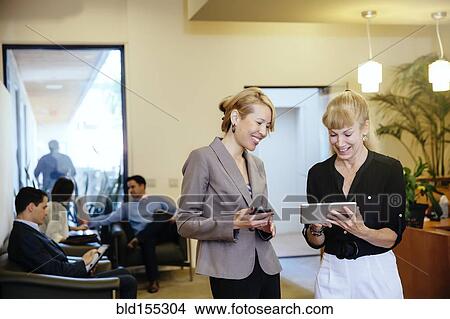 Picture - Businesswomen using digital tablet in office hallway. Fotosearch