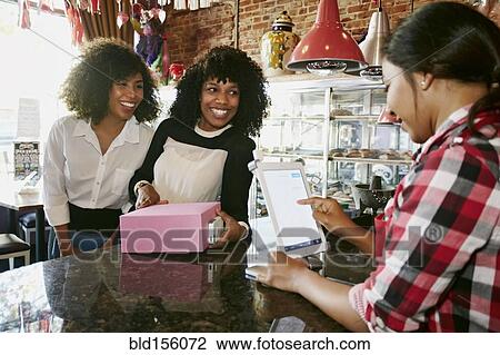 Stock Image - Cashier serving customers with digital tablet register in bakery. Fotosearch