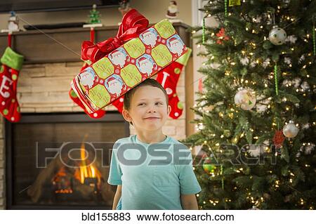 Stock Image - Caucasian boy balancing Christmas gift on head. Fotosearch