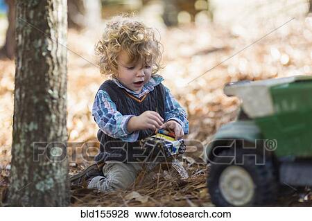 Stock Photo - Caucasian boy playing with toy trucks in forest. Fotosearch