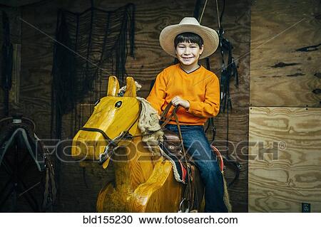 Stock Image - Caucasian boy riding toy wooden horse. Fotosearch