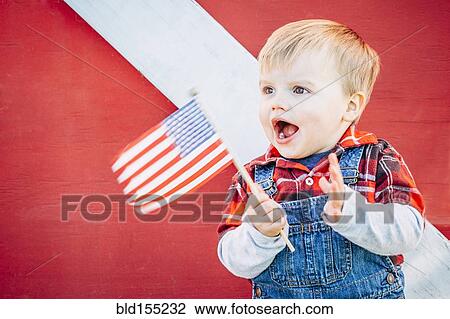 Stock Image - Caucasian boy waving American flag outside barn. Fotosearch