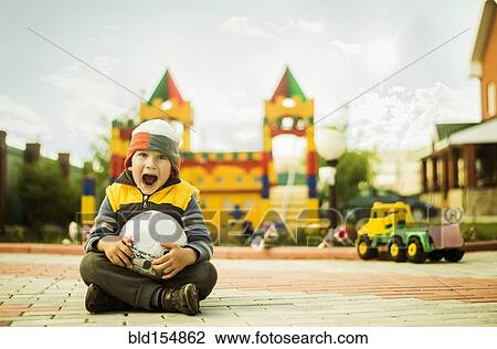 Stock Image - Caucasian boy with mouth open holding ball at playground. Fotosearch
