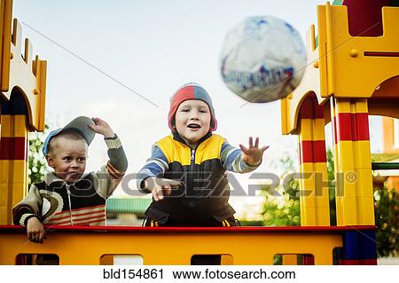 Stock Image - Caucasian boys throwing ball in playground. Fotosearch