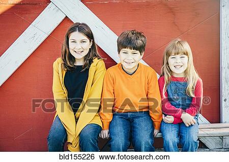Stock Photograph - Caucasian brother and sisters smiling on farm. Fotosearch
