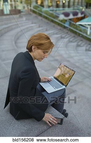 Stock Photo - Caucasian businesswoman using cell phone and laptop in city park. Fotosearch