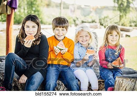 Picture - Caucasian children eating watermelon outdoors. Fotosearch