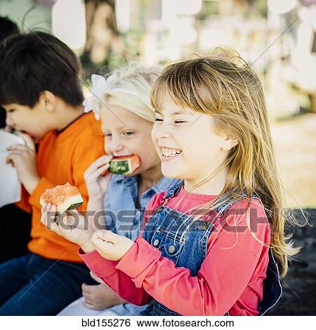 Stock Photograph - Caucasian children eating watermelon outdoors. Fotosearch